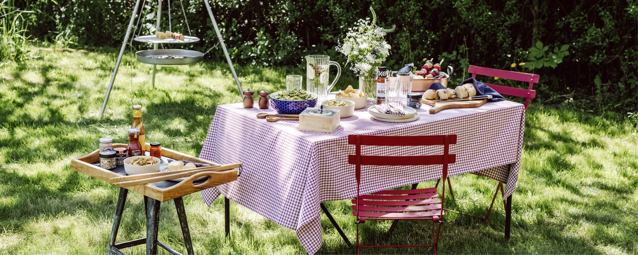 Sommerlich gedeckter Grilltisch mit Schwenkgrill im Hintergrund