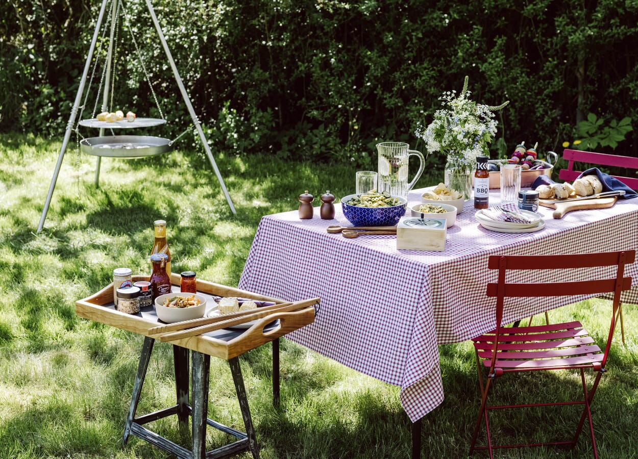 Sommerlich gedeckter Grilltisch mit Schwenkgrill im Hintergrund